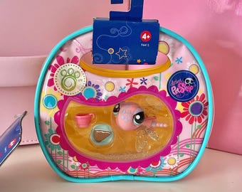 May include: A Littlest Pet Shop toy in a pink and blue package. The package features a pink and yellow floral design, with a pink toy inside. The package has a blue cardboard hanger with the number 4+.