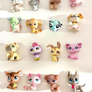 Puede incluir: Colección de pequeñas figuras de animales de plástico de colores, incluyendo perros, gatos, un ratón y un conejo. Las figuras tienen ojos grandes y están en varias poses, con diferentes colores y patrones.
