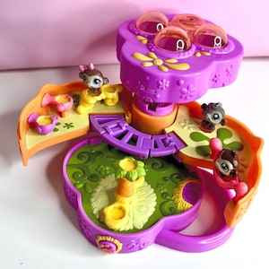 Puede incluir: Un juego de juguetes morado y naranja con una parte superior en forma de flor y varias figuras de animales pequeños. El juego tiene un tema de jardín con detalles en verde y amarillo. La parte superior presenta cúpulas transparentes y detalles de flores amarillas.