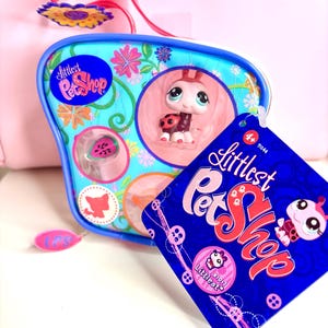 Puede incluir: Un juego de juguetes Littlest Pet Shop con una figura de mariquita en una caja azul y rosa. La caja tiene diseños florales y el logotipo de la marca. Una etiqueta azul con el nombre de la marca y un gráfico de mariquita está adjunta.