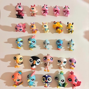 Puede incluir: Una colección de pequeñas figuras de animales de plástico de colores, incluyendo pájaros, abejas y otras criaturas. Los juguetes están en varias poses y colores, con ojos grandes y expresivos. Las figuras están dispuestas sobre una superficie blanca.