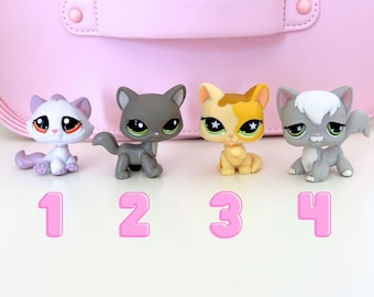 May include: Four small, colorful cat figurines with large eyes are arranged in a row. The cats are in various poses and colors, including gray, white, and yellow. Pink numbers 1 through 4 are below the cats. A pink background is behind the cats.