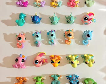 May include: A selection of small, brightly coloured plastic animal figurines, including frogs, fish, and seahorses. The toys are in various colours such as pink, blue, yellow, and orange. The figurines are arranged on a white surface.