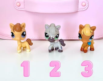 Pode incluir: Três cavalos de brinquedo em tons de bege, cinza e castanho, com olhos grandes e pequenas crinas. Os brinquedos estão numerados 1, 2 e 3 em rosa. O fundo é rosa claro, com uma pega rosa a condizer.