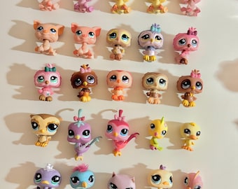 May include: A collection of colorful, small plastic animal figurines, including pigs and owls. The figurines are in various colors, such as pink, yellow, purple, and brown. Each figurine has large eyes and unique details.