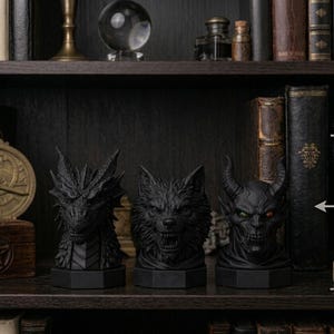 Pode incluir: Tr&ecirc;s bustos negros de fantasia, um drag&atilde;o, um lobo e um dem&oacute;nio, cada um com cerca de 12 cm de altura, s&atilde;o exibidos numa prateleira. O drag&atilde;o tem escamas detalhadas, o lobo mostra os dentes e o dem&oacute;nio tem chifres e olhos brilhantes. A prateleira &eacute; rodeada por livros e objetos decorativos.