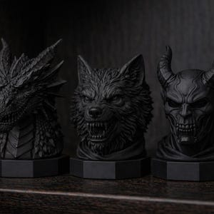 Pode incluir: Tr&ecirc;s bustos negros de fantasia: um drag&atilde;o, um lobo e um dem&ocirc;nio com chifres. Cada escultura &eacute; intrincadamente detalhada e montada em uma base hexagonal. O drag&atilde;o tem espinhos afiados, o lobo mostra os dentes e o dem&ocirc;nio tem uma express&atilde;o amea&ccedil;adora.