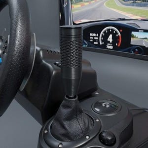 Pode incluir: Uma configuração de simulador de corrida preta com volante, alavanca de câmbio e um monitor exibindo uma pista de corrida. A alavanca de câmbio tem uma pega texturizada. O monitor mostra a velocidade do carro em 4 e as RPM em 7800.