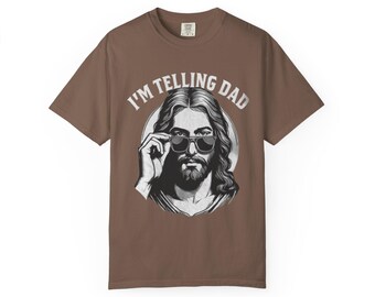 May include: Brown t-shirt featuring a graphic of a person wearing sunglasses, with the text "I'M TELLING DAD" in white. The graphic is a black and white illustration. The shirt is a solid brown color.