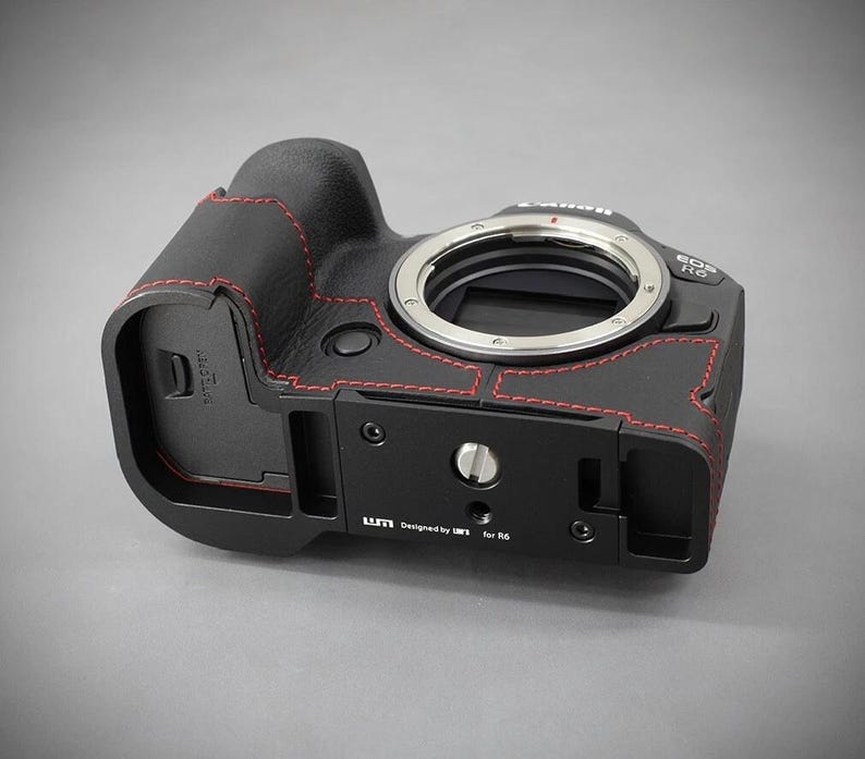 Puede incluir: Cuerpo de c&aacute;mara negro con costuras rojas y montura de lente plateada. La c&aacute;mara tiene una placa base negra con el texto "Designed by LM3 for R6". Se muestra una c&aacute;mara Canon EOS R6.