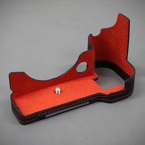 Puede incluir: Funda de c&aacute;mara negra y roja con interior texturizado. La funda tiene un exterior negro con costuras rojas y un interior rojo. Un tornillo plateado es visible en la base. La funda est&aacute; dise&ntilde;ada para proteger una c&aacute;mara.