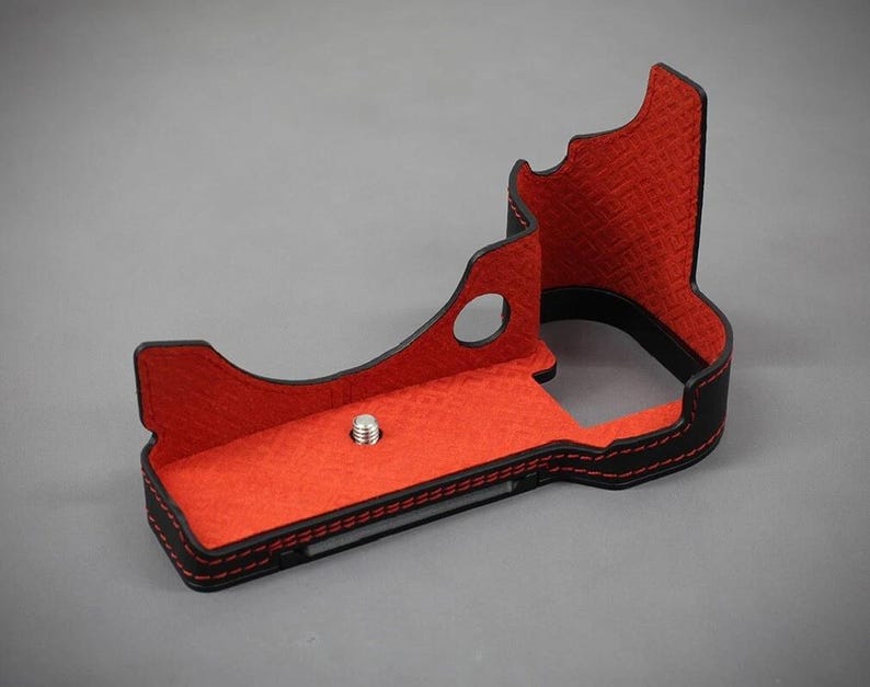 Puede incluir: Funda de c&aacute;mara negra y roja con interior texturizado. La funda tiene un exterior negro con costuras rojas y un interior rojo. Un tornillo plateado es visible en la base. La funda est&aacute; dise&ntilde;ada para proteger una c&aacute;mara.