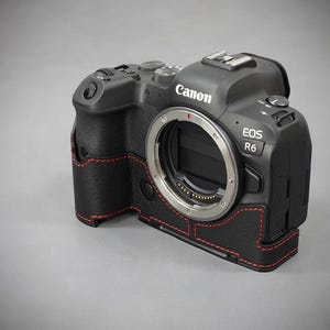 Puede incluir: C&aacute;mara Canon EOS R6 negra con funda de cuero y costuras rojas. La c&aacute;mara tiene una montura de lente plateada y varios botones y diales. La funda envuelve el cuerpo de la c&aacute;mara.
