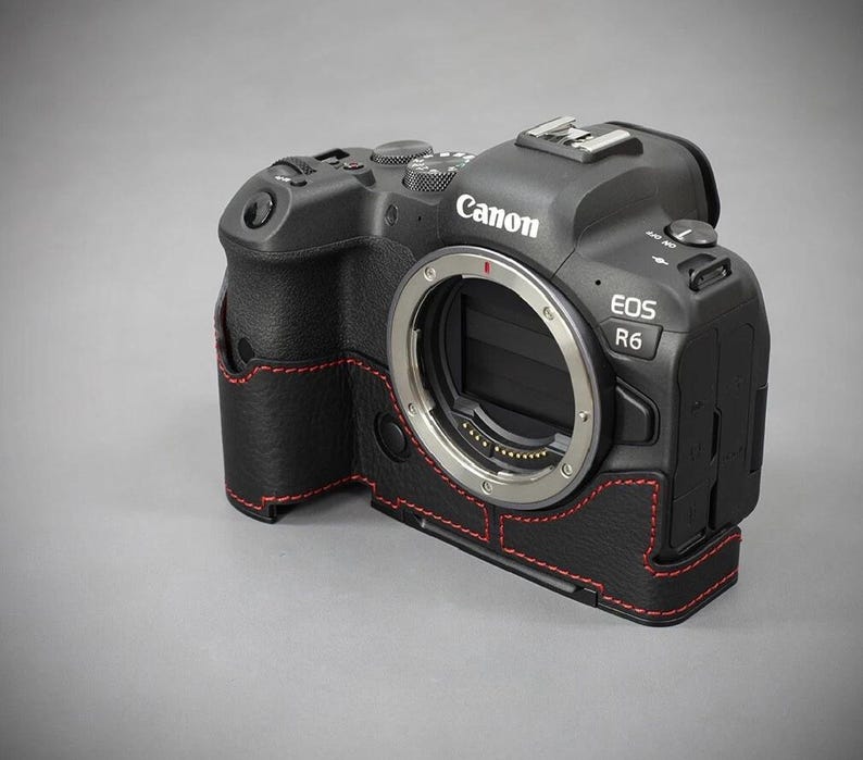 Puede incluir: C&aacute;mara Canon EOS R6 negra con funda de cuero y costuras rojas. La c&aacute;mara tiene una montura de lente plateada y varios botones y diales. La funda envuelve el cuerpo de la c&aacute;mara.