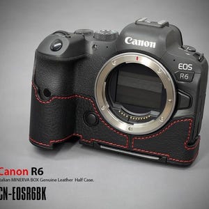 Puede incluir: C&aacute;mara Canon EOS R6 negra con una media funda de cuero. La funda tiene costuras rojas y cubre la base y el agarre de la c&aacute;mara. El logotipo de Canon y el nombre del modelo EOS R6 son visibles. El texto "CN-EOSR6BK" tambi&eacute;n est&aacute; presente.
