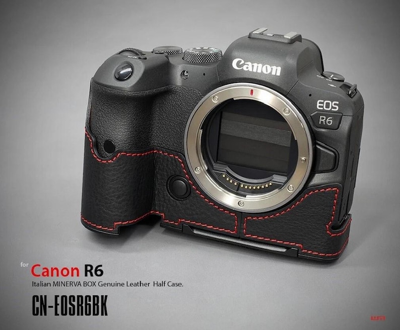 Puede incluir: C&aacute;mara Canon EOS R6 negra con una media funda de cuero. La funda tiene costuras rojas y cubre la base y el agarre de la c&aacute;mara. El logotipo de Canon y el nombre del modelo EOS R6 son visibles. El texto "CN-EOSR6BK" tambi&eacute;n est&aacute; presente.