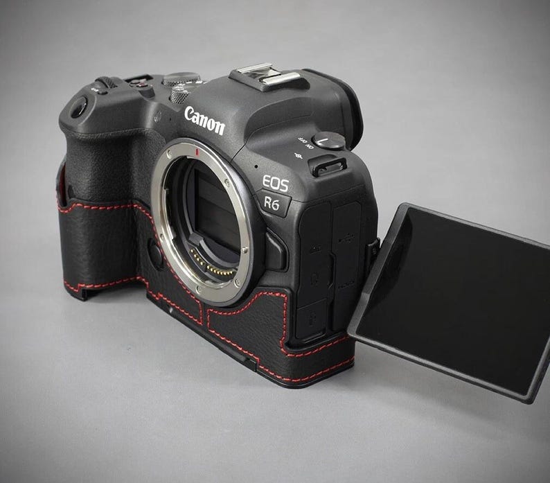 Puede incluir: C&aacute;mara Canon EOS R6 negra con funda de cuero y costuras rojas. La c&aacute;mara tiene una montura de lente, una pantalla abatible y el logotipo de Canon. La funda envuelve el cuerpo de la c&aacute;mara.
