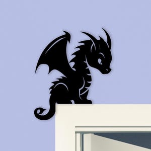 May include: A black dragon silhouette with detailed wings, horns, and a curled tail. The dragon is perched on a white surface against a light blue background. This decorative item is suitable for wall decor.