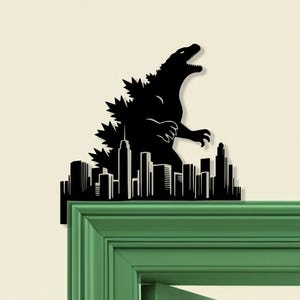May include: Black silhouette of Godzilla towering over a city skyline. The design is mounted on a green door frame, creating a striking contrast. The artwork captures the iconic monster in a dynamic pose, with the city below.