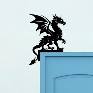 May include: Black dragon silhouette with detailed wings, claws, and a spiked tail. The dragon is perched on a corner, with a blue door frame in the background. The dragon is a decorative item.