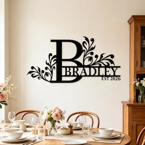 May include: A black metal wall sign featuring a large capital letter B with decorative floral flourishes extending from the sides. The name BRADLEY is integrated into the letter, with the text EST 2026 positioned underneath the name.