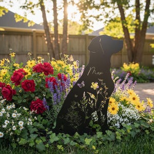 May include: Black metal silhouette of a Labrador Retriever dog, sitting in a garden. The dog's outline is filled with floral and butterfly cutouts. The name "Max" is written on the dog's side. The garden features red roses, yellow daisies, and purple lavender.