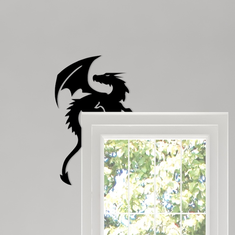 May include: A black dragon silhouette with outstretched wings and a long tail. The dragon is positioned above a white window frame, with a view of green foliage visible through the window.