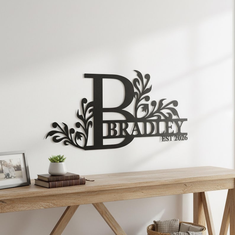 May include: A black metal wall sign featuring a large capital letter B with decorative floral scrollwork extending from the sides. The name BRADLEY is integrated into the design, accompanied by the text EST 2026 in a clean, sans-serif font.