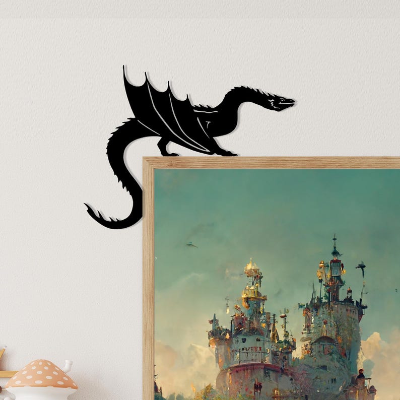 May include: A black metal dragon silhouette decorates the corner of a framed artwork. The dragon has outstretched wings and a long tail. The artwork features a fantasy castle scene with a teal sky.