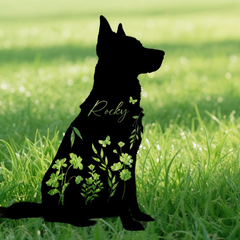 May include: A black silhouette of a dog sitting in profile, filled with green floral and butterfly designs. The name "Rocky" is written in a cursive font on the dog's side. The background is a blurred green field.