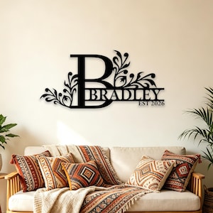 May include: A black metal wall sign featuring a large capital letter B integrated with decorative floral scrollwork. The name BRADLEY is displayed in a horizontal line across the letter, with the text EST 2026 positioned below it.