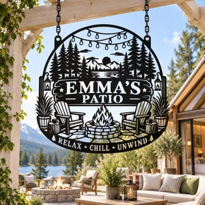 May include: A circular black metal sign featuring a laser-cut design of a forest, mountains, a fire pit, and two chairs. The text reads EMMA'S PATIO and RELAX CHILL UNWIND. The sign is suspended by two black chains from a wooden beam structure.