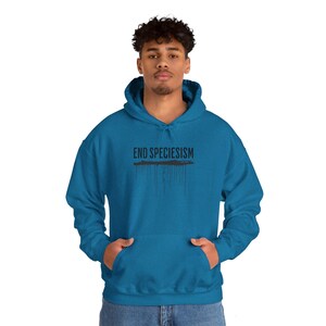 Op de afbeelding: Een blauw hoodie met de tekst "END SPECIESISM" in zwarte letters met zwarte verf die van de letters druipt.
