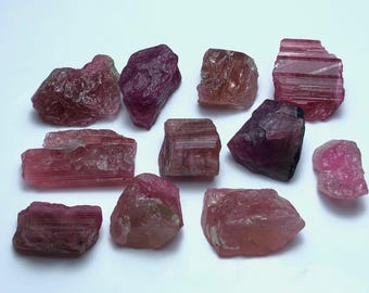 May include: A collection of raw, uncut tourmaline crystals in shades of pink and red. The gemstones vary in size and shape, with visible textures and natural formations. Ideal for collectors or jewelry making.