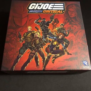 May include: A G.I. Joe Mission Critical board game box featuring a red, white, and blue logo with the text "G.I. JOE MISSION CRITICAL". The box art features a group of action figures in a comic book style, including a black-clad figure with a sword, a female figure in a yellow and blue costume, and a male figure in a green military uniform.