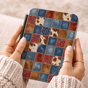 May include: A rectangular case with a patchwork design. The case features squares of denim blue, brown, red paisley, and cowhide print. The case is held in the hands of a person wearing a cream-colored sweater.