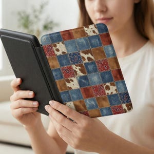 May include: A black e-reader case with a patchwork design. The cover features squares of denim, paisley, cowhide, and solid colors in red, brown, and blue. The case is open, revealing the e-reader screen.