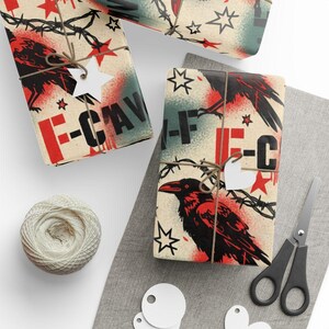 以下が含まれることがあります： 黒いカラス、有刺鉄線、赤い星、赤と黒の文字「F-CAV」を特徴とするヴィンテージデザインのギフト包装。 ギフトは紐で結ばれ、白い星型のタグで飾られています。 紐のボールとハサミも存在します。