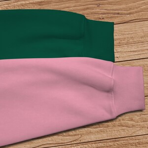 May include: A two-toned sweatshirt with a dark green top and a light pink bottom. The sweatshirt has a ribbed cuff on the sleeve.