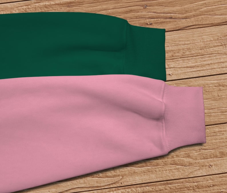 May include: A two-toned sweatshirt with a dark green top and a light pink bottom. The sweatshirt has a ribbed cuff on the sleeve.