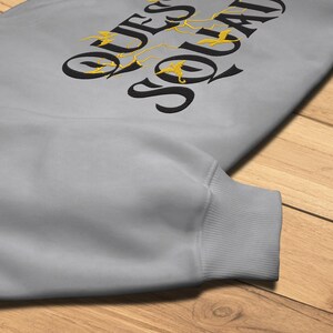 May include: A gray sweatshirt with the text "QUESO SOLADO" in black with gold bird silhouettes.