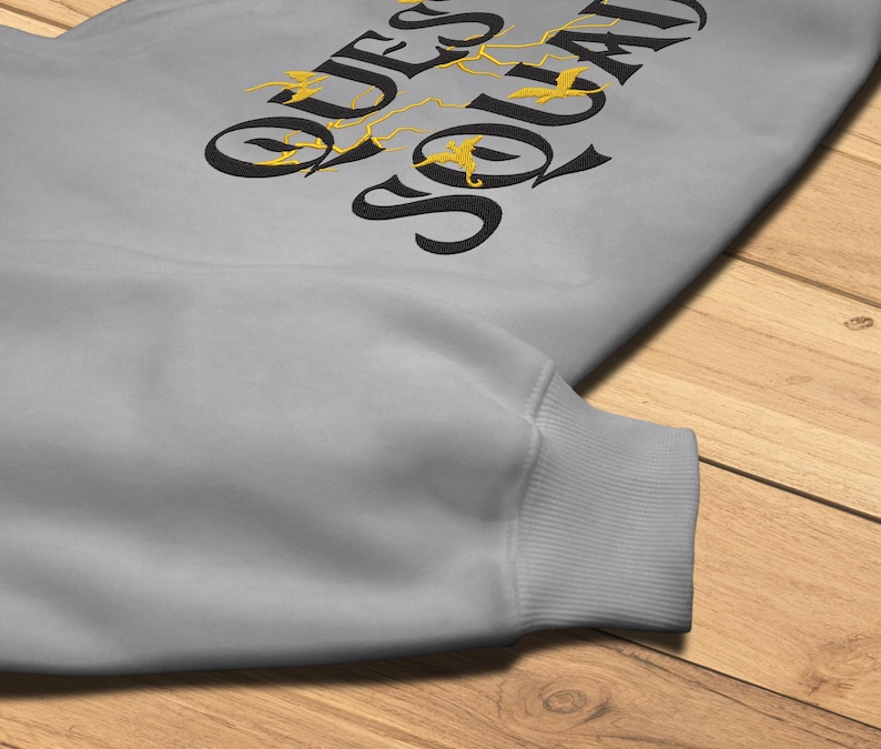 May include: A gray sweatshirt with the text "QUESO SOLADO" in black with gold bird silhouettes.