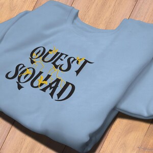 May include: A light blue sweatshirt with the text "QUEST SQUAD" in black lettering with gold accents.
