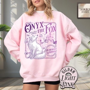 Może przedstawiać: Jasnor&oacute;żowa bluza z fioletową grafiką lisa, napisem "Onyx the Fox" i "The Bravest Warrior". Projekt zawiera motyle i zamek. Bluza to Gildan Light Pink.