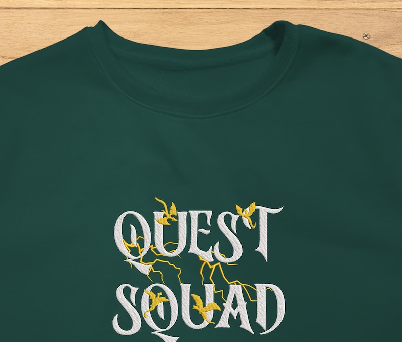 May include: A dark green sweatshirt with the text "QUEST SQUAD" in white lettering with yellow accents. The text is in a stylized font.