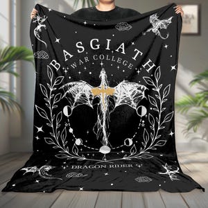 May include: Black blanket with a white and gold dragon and celestial design. The blanket features the text "BASGIATH WAR COLLEGE" and "DRAGON RIDER". The design includes a dragon, stars, clouds, and a moon phase circle.