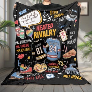 Op de afbeelding: Zwarte fleece deken met diverse afbeeldingen en tekst, waaronder hockeytruien, een ijsvogel en de woorden "Heated Rivalry". De deken bevat zinnen als "We didn't even kiss" en "I'm coming to the cottage."