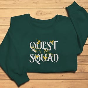 May include: A dark green sweatshirt with the text "QUEST SQUAD" in white lettering with yellow floral accents.