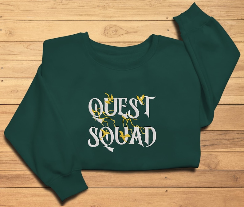 May include: A dark green sweatshirt with the text "QUEST SQUAD" in white lettering with yellow floral accents.