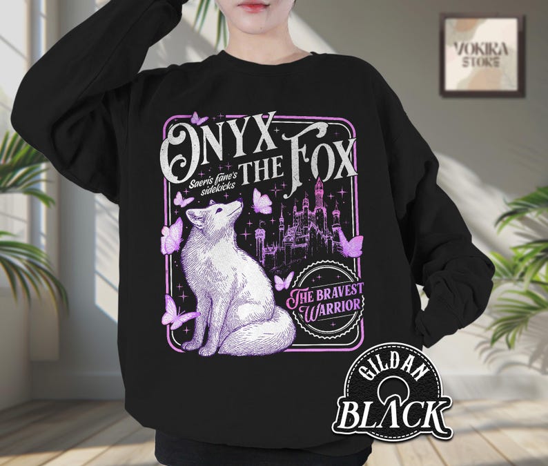 Może przedstawiać: Czarna bluza z ilustracją białego lisa, napisem "Onyx the Fox" i "The Bravest Warrior". Projekt zawiera zamek i fioletowe motyle. Bluza to Gildan Black.